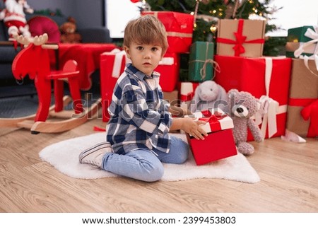 Adorable hispanic boy unpacking gift sitting by christmas tree at home