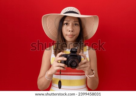 Middle age chinese woman using reflex camera wearing summer hat skeptic and nervous, frowning upset because of problem. negative person. 