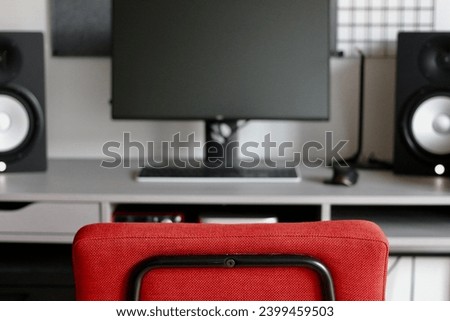 Abstract photo of a minimalist desk setup with studio speakers and a monitor, with a splash of red from the office chair