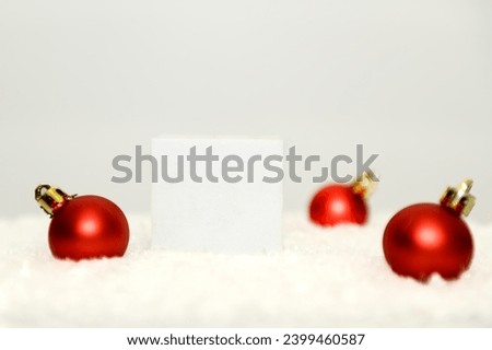 White square podium with red Christmas balls. On white artificial snow.