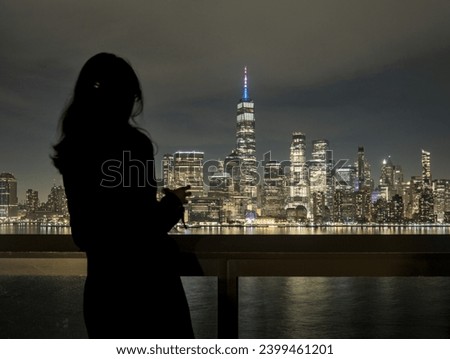 woman looking at downtown manhattan nyc skyline (after sunset, night time)  world trade center cityscape (high rise urban buildings) railing, hudson river, waterfront, bay, harbor new york city view