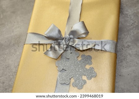 Elegant gift wrapping idea for Christmas. A gift wrapped with gold paper, a silver shiny bow an a glittery snowflake gift tag.