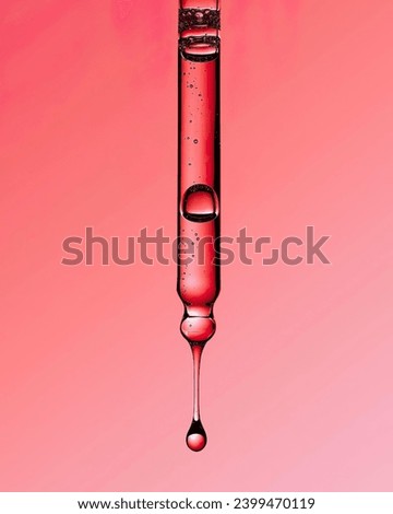 Liquid red oil serum drop in pipette isolated on red background. Peeling, aha acid, collagen skincare fluid, close up photo with shallow depth of field. Transparent crimson essence in dropper.