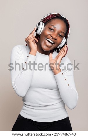 Smiley adorable cute attractive African American woman in casual stylish outfit wearing wireless headphones headset singing while listening to favourite songs posing in studio isolated.