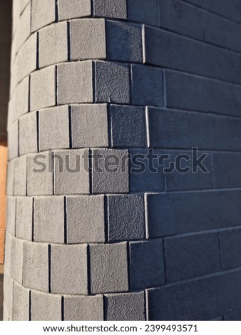 round corner of the building lined with tiles in an arch. the shadows highlight the textures and distortions of the gray mosaic of the wall