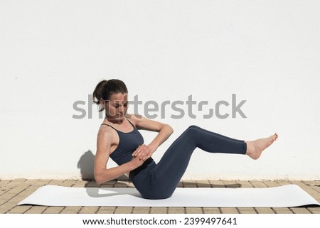 Sporty woman doing a twisted boat pose core exercise Royalty-Free Stock Photo #2399497641