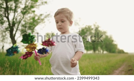 baby boy playing with spinner toy in the park. happy family kid dream concept. baby a son plays with a toy windmill outdoors in the forest lifestyle in summer Royalty-Free Stock Photo #2399499343