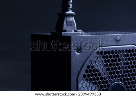 Modern computer AC power supply unit with a powerful fan and a connected power cable on a dark background. Fragment. A device for power supply of a modern personal computer. Photo. Close-up Royalty-Free Stock Photo #2399499353