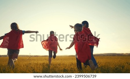 team of kids superheroes run. happy family kid concept. a group of children playing superheroes in capes and masks run through the grass at sunset. success business striving for goal dream concept Royalty-Free Stock Photo #2399506739