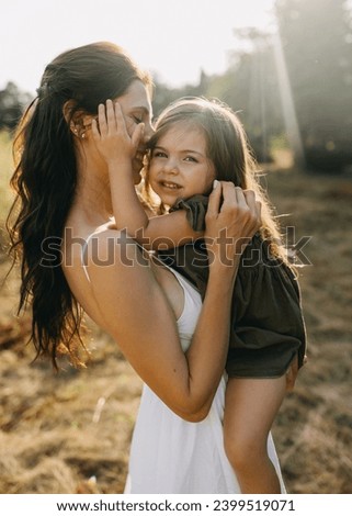 Portrait of a mother holding her little daughter in arms, outdoors, smiling.