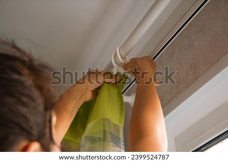 A hostess is hanging curtains by attaching them to a cornice, adding a decorative touch to a home interior. This scene captures the process of enhancing home decor.