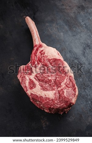 Raw dry aged wagyu tomahawk steak offered as close-up on an old black rustic board with copy space 