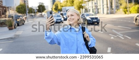 Image of smiling young woman, modern girl with smartphone, taking selfie, shooting a picture of busy city streets, recording video outdoors.