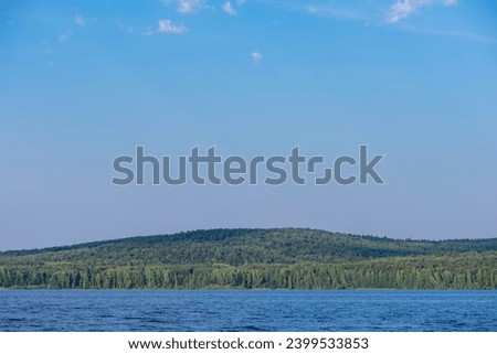 Beautiful summer landscape with a river near a green forest on a blue sky background. Natural desktop background.