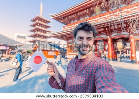 Handsome young tourist enjoying summer holiday in Tokyo, Japan - Traveling life style concept with smiling man taking selfie on city street with japan flag- Tourism and summertime vacation concept