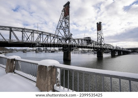 Hawthorne Bridge viewed from the west bank of the Willamette River in Portland, Oregon, after snowfall in winter. The truss bridge is the oldest vertical-lift bridge in operation in the United States.