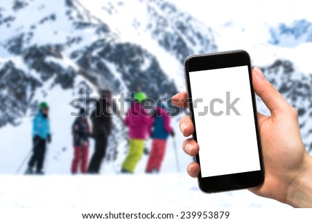 smartphone in the hands of a woman and a group of people on skis