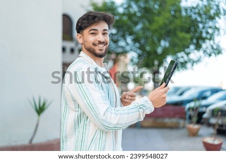 Handsome Arab man holding a tablet at outdoors and pointing it