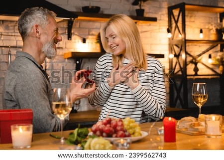 Surprised woman being proposed by her mature boyfriend on a date in the kitchen. Proposal, engagement, ring for wedding, new family start concept. She said yes Royalty-Free Stock Photo #2399562743