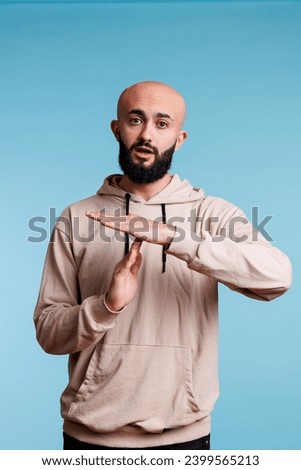 Young arab man taking break while showing time out gesture portrait. Person in casual hoodie clothes stopping communication with interruption signal and looking at camera