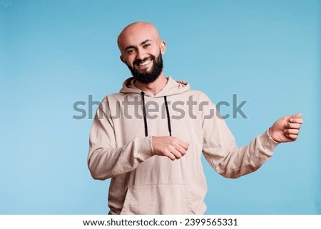 Cheerful arab man promoting product and holding invisible banner for ads portrait. Smiling person pretending to carry placard in two hands and looking at camera with happy expression
