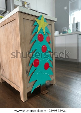 Interior photo view of a samll Christmas tree made from cardboard DIY by kids children painted in green with red balls and wire gardlands as a sustain xmas decoration for season's greedings for family