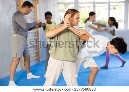 Tweens attending self-defense classes under careful supervision of instructor at training center. Focused girl applying armlock technique in sparring with boy Royalty-Free Stock Photo #2399580833