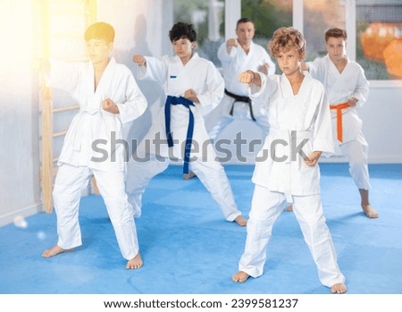 Focused teenage boy with group of karate practitioners wearing white kimonos diligently performing kata routines to hone martial arts skills in training room