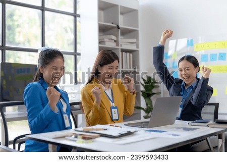Team of young Asian business woman using laptop computer in the office, getting good news, feeling joy, laughing, making winner gesture, happy to win prize. Royalty-Free Stock Photo #2399593433