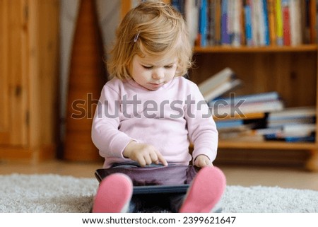 Cute little toddler girl playing with tablet pc at home. Healthy baby touching pad with fingers, looking cartoons and having fun with educational games on computer. Early development concept