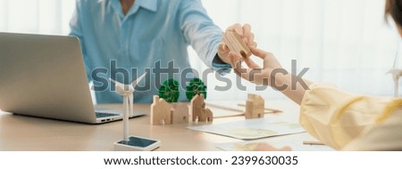 Two business people talking about eco city at green business meeting on meeting table with windmill represented renewable energy, wooden house block and tree model represent green city. Delineation. Royalty-Free Stock Photo #2399630035