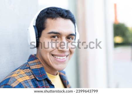 Close-up portrait of a happy student listening to music outdoors leaning on a urban wall