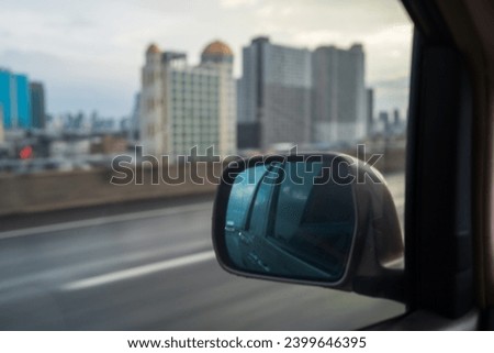 View from side mirror of car, sky with buildings at  Highway.
