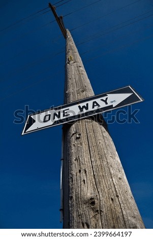 One Way Sign on Weathered Utility Pole Against Clear Blue Sky