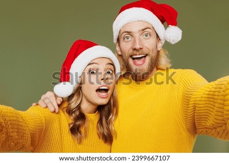 Close up merry young couple two friends man woman wear sweater Santa hat posing doing selfie shot pov on mobile cell phone isolated on plain green background. Happy New Year Christmas holiday concept