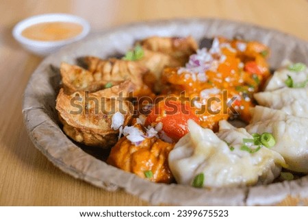 A plate of assorted chicken momos (steamed, fried and chilli sauce dumplings) served on a leaf plate at Tapari Nights, a Nepalese restaurant in Auburn, Sydney - NSW, Australia Royalty-Free Stock Photo #2399675523