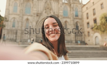 Traveler girl making video call from smartphone, waving hand in greeting at the old building in the historical part of the old European city background
