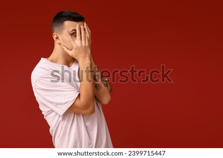 Handsome ashamed young man covering face with hands on red background Royalty-Free Stock Photo #2399715447