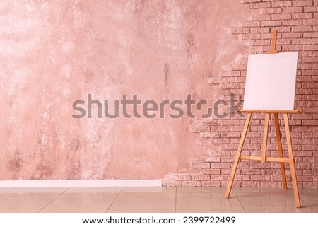 Wooden easel with blank canvas near color brick wall