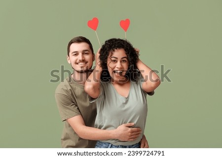 Funny young couple with paper hearts for Valentine's day on green background Royalty-Free Stock Photo #2399724791