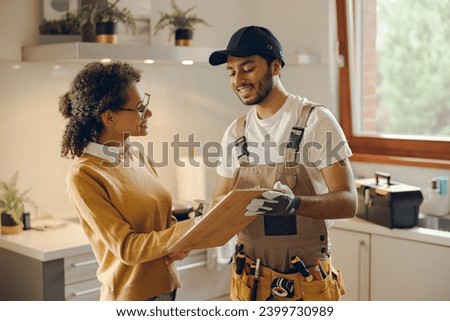 Smilng young woman signing document while communicating with handyman at the kitchen Royalty-Free Stock Photo #2399730989