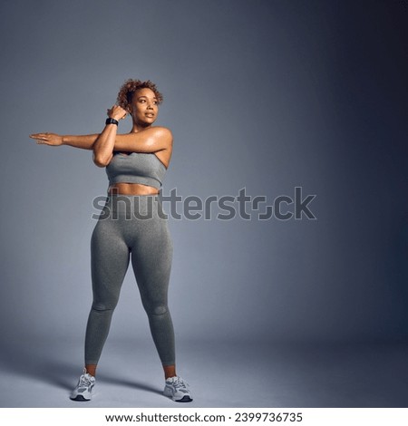 Studio Shot Of Woman In Gym Fitness Clothing Wearing Fitness Tracker Stretching On Grey Background