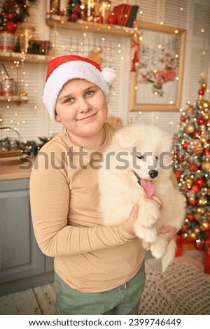 Christmas at home. Children and Samoyed puppies under the Christmas tree. Small children in a Santa hat hug a pet and open Christmas presents. Children are playing with an animal.
