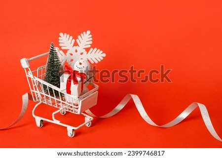 White shopping cart with Christmas decorations on red background, copy space