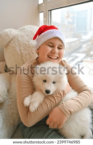 Christmas at home. Children and Samoyed puppies under the Christmas tree. Small children in a Santa hat hug a pet and open Christmas presents. Children are playing with an animal. 