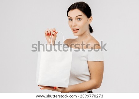 Happy woman with a white bag in her hands on a light background. Charismatic, positive woman enjoying a discount and shopping. Shopping, delivery and gifts concept.