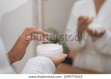 Elevating beauty: In a bathroom close-up, a woman clutches a jar of rejuvenating cream, enhancing her skincare routine. 