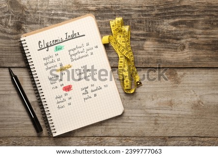 List with products of low, moderate and high glycemic index in notebook, marker and measuring tape on wooden table, flat lay. Space for text Royalty-Free Stock Photo #2399777063