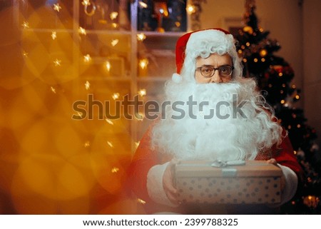 
Happy Santa Claus Holding a Present in Front of the Tree. Cheerful Santa delivering and offering Christmas gifts 
