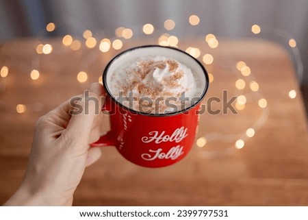 Red Christmas mug with cocoa and whipped cream in a girl's hand